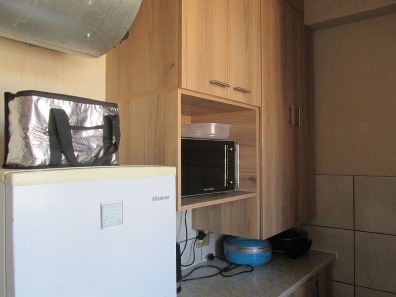 A functional kitchen area featuring light wood-toned cabinetry, a tiled backsplash, and a compact countertop workspace with an integrated extractor fan.