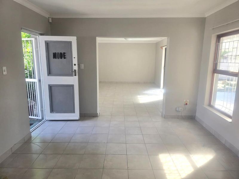 An empty, open-plan living area featuring neutral tiled flooring, coved cornicing, and direct access to the exterior via a security gate.