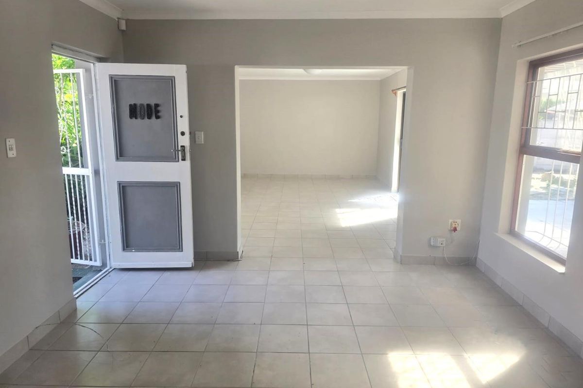 An empty, open-plan living area featuring neutral tiled flooring, coved cornicing, and direct access to the exterior via a security gate.
