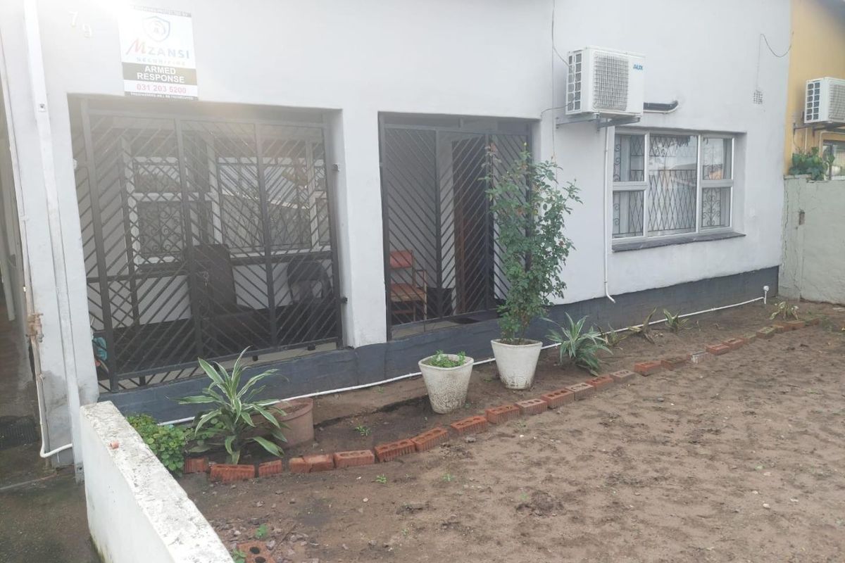 Rear exterior view of the property featuring security gates, burglar bars, and an installed air conditioning unit with an unlandscaped garden area.