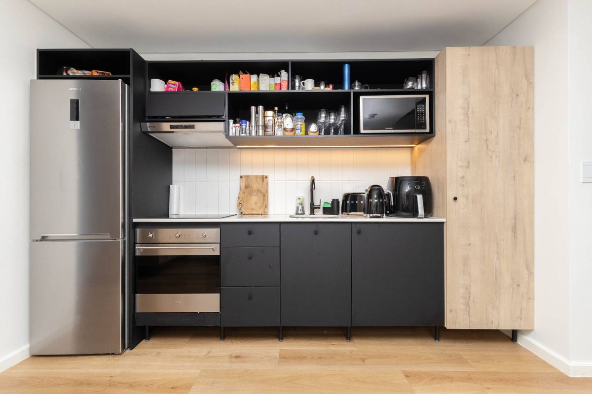 Modern compact kitchen featuring matte black cabinetry, light wood-look pantry, integrated stainless steel oven, extractor fan, and subway tile backsplash.