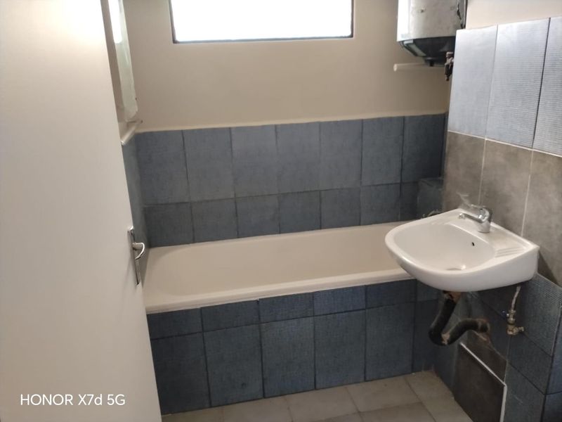 A compact bathroom featuring a bathtub, wall-mounted basin, and blue tiled splashback, requiring cosmetic updates and plumbing finishing.