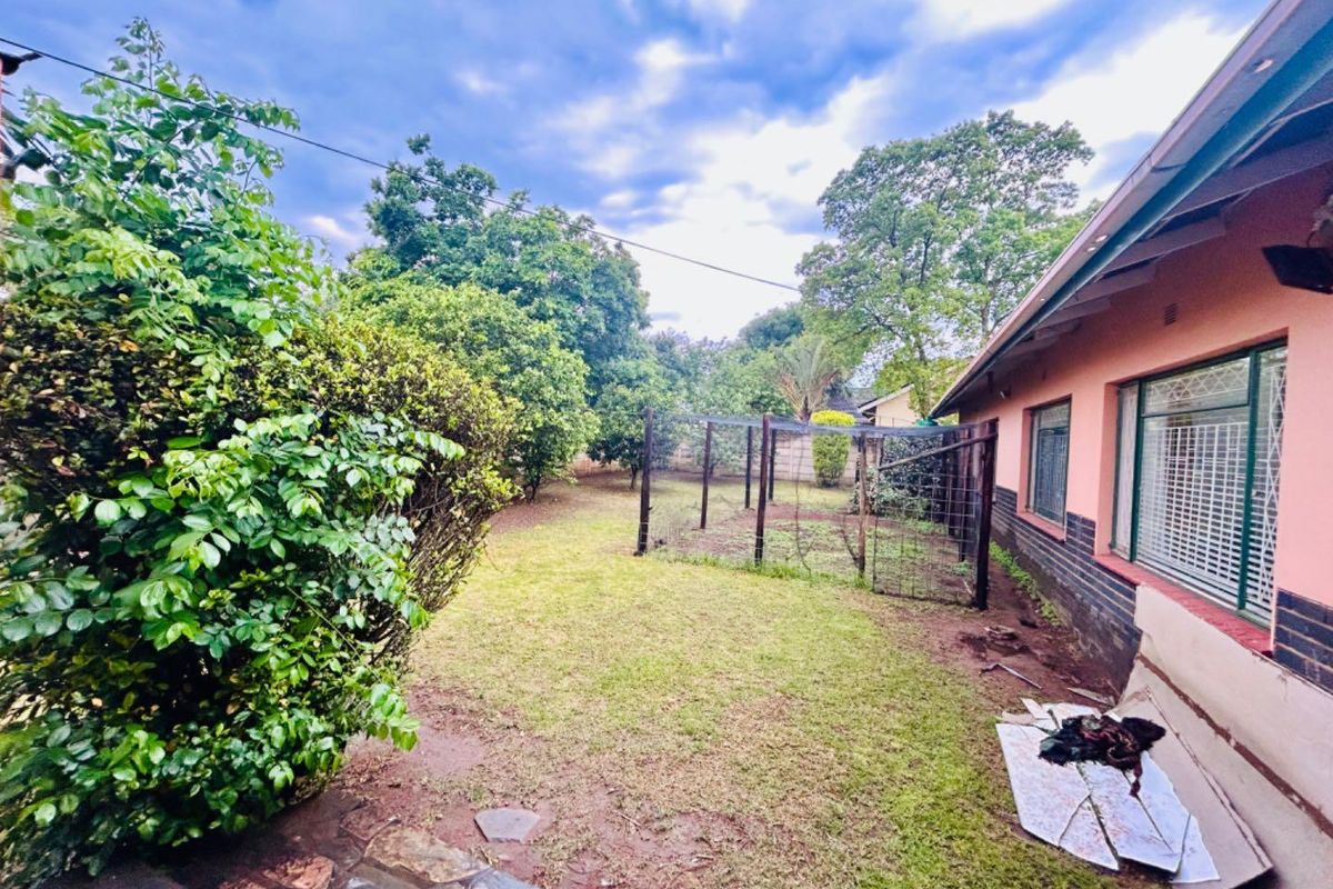 A rear garden area featuring a lawn, mature trees, and a fenced enclosure, adjacent to the side of the house.
