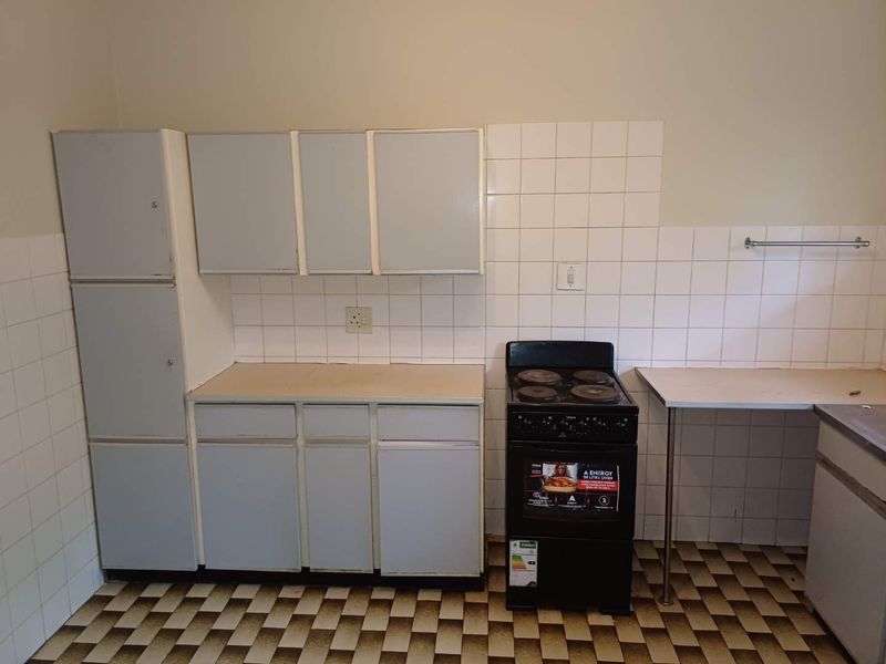 A functional kitchen area featuring built-in cabinetry, a tiled splashback, and a freestanding stove, offering potential for modernization and aesthetic updates.