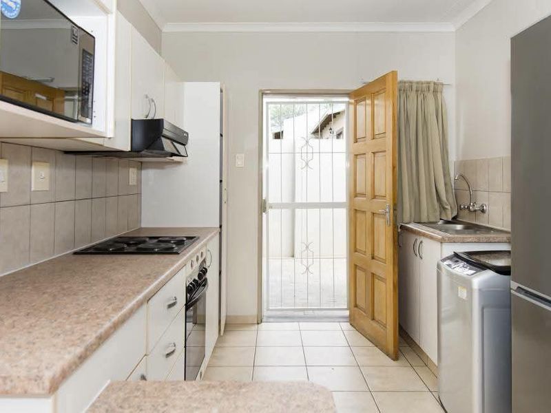 Functional kitchen featuring built-in cabinetry, electric hob, oven, and direct access to an exterior area through a security gate.