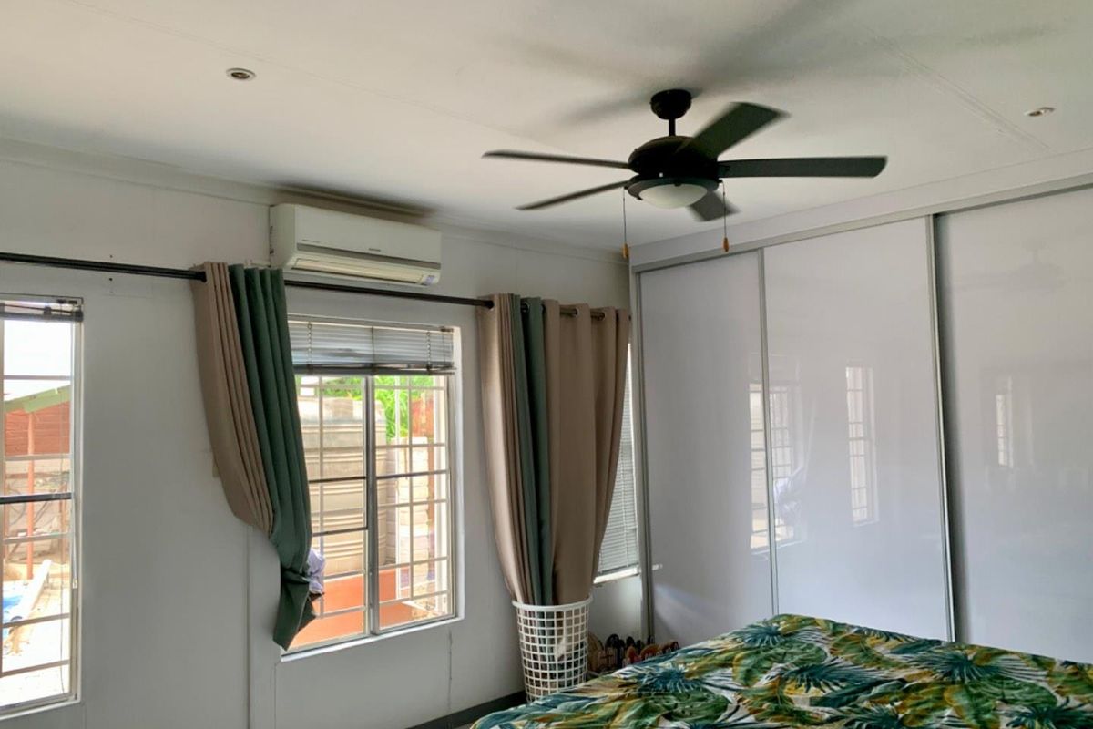 A bedroom featuring built-in sliding door wardrobes, a ceiling fan, and a wall-mounted air conditioning unit.