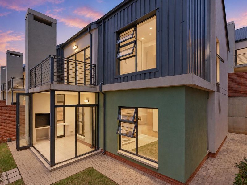 Modern double-storey cluster home featuring a paved rear patio, built-in braai, balcony, and contemporary metal and plaster facade finishes.