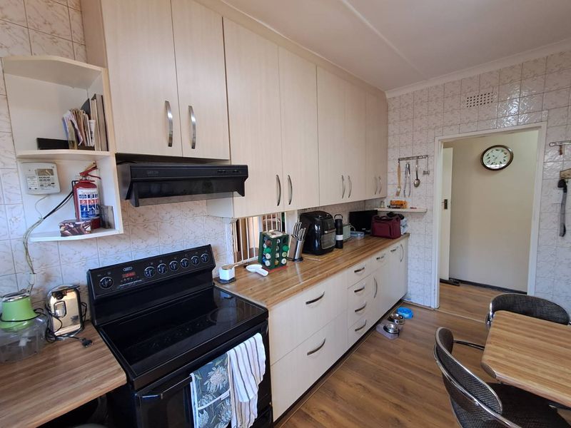 A functional kitchen featuring light-toned built-in cabinetry, laminate countertops, a tiled splashback, and a freestanding stove with an extractor fan.