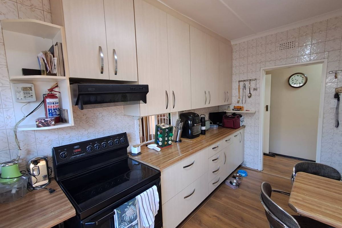 A functional kitchen featuring light-toned built-in cabinetry, laminate countertops, a tiled splashback, and a freestanding stove with an extractor fan.