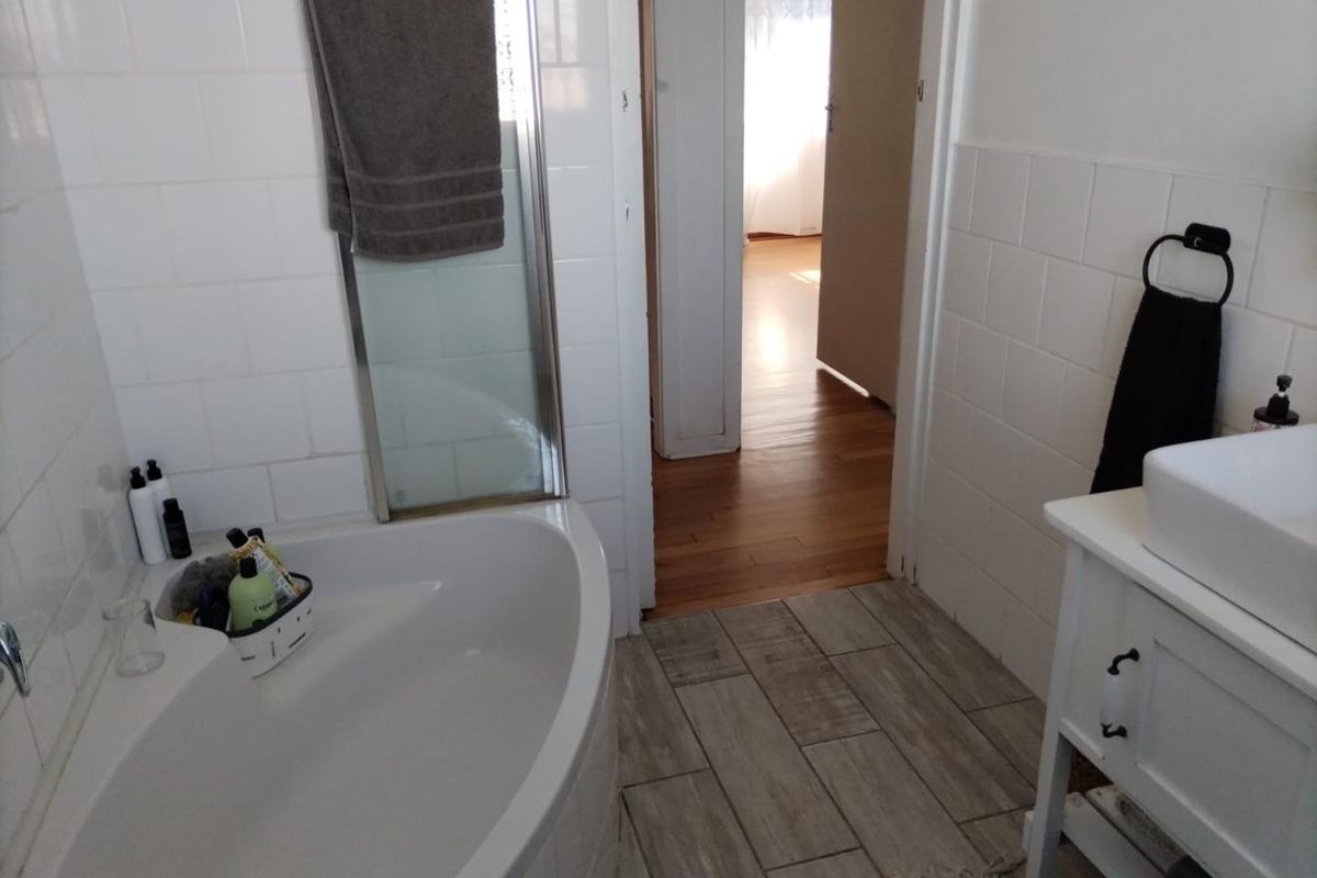 A functional bathroom featuring a corner bathtub, shower enclosure, and a vanity unit with modern wood-look floor tiling and white wall tiles.