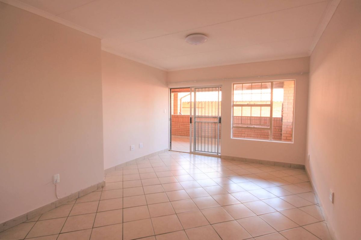 An empty, well-lit living room featuring neutral tiled flooring and a sliding glass door providing access to an outdoor balcony area.
