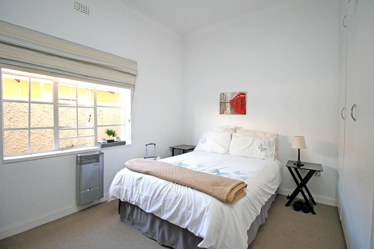 A well-lit bedroom featuring neutral carpeting, built-in wardrobe storage, and a wall-mounted heater beneath the window.