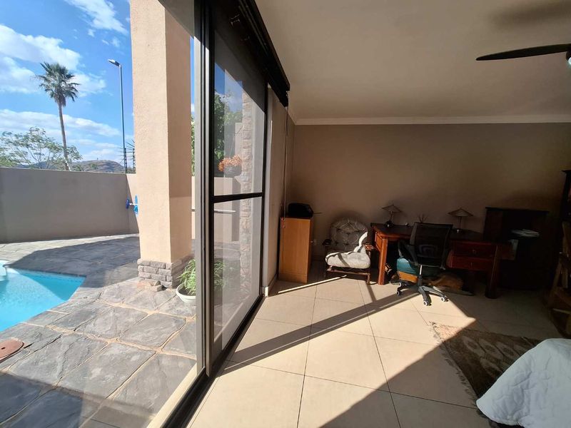 Covered patio area featuring large sliding glass doors, tiled flooring, and direct access to an outdoor swimming pool and paved deck.