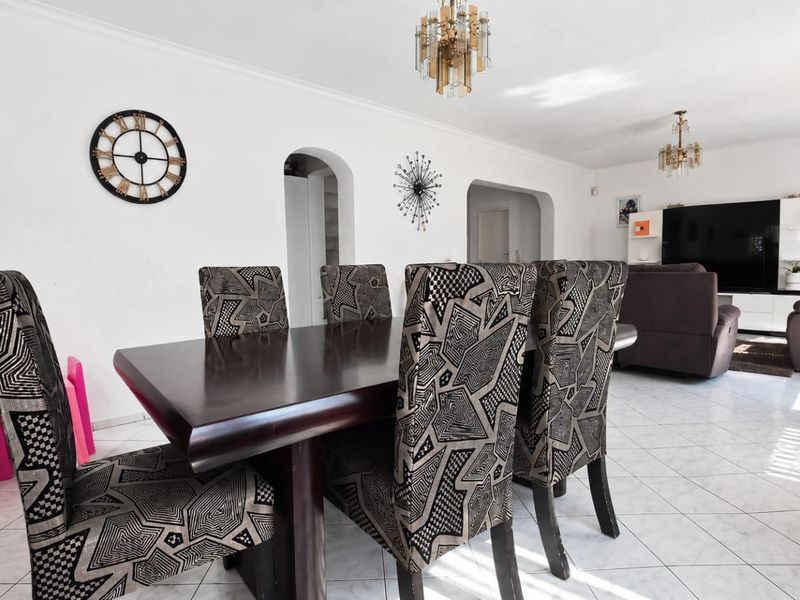Spacious open-plan living and dining area featuring tiled flooring, decorative archways, and classic ceiling light fixtures in a bright, neutral setting.