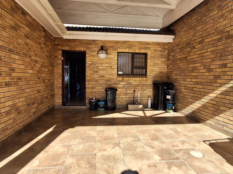 A covered outdoor patio area featuring exposed brick walls and tiled flooring, providing a functional space for outdoor living.