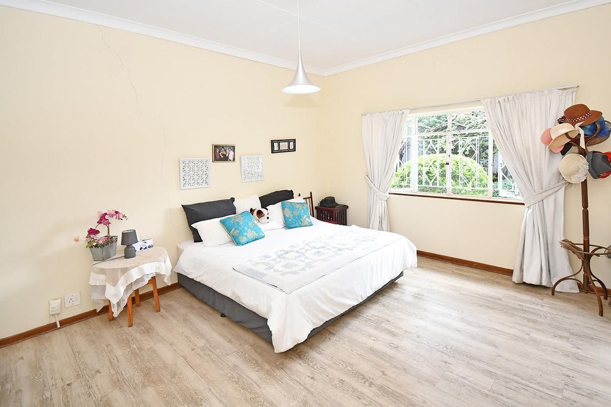 A spacious bedroom featuring light-toned wood-look flooring, a large window with security bars, and neutral wall finishes.
