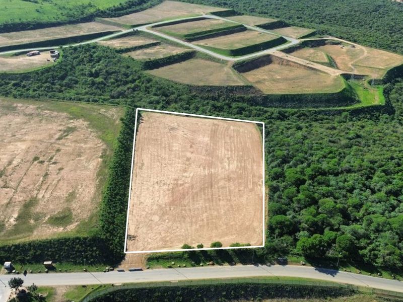 Aerial view of a cleared industrial plot with direct road access, surrounded by natural vegetation and adjacent development infrastructure.