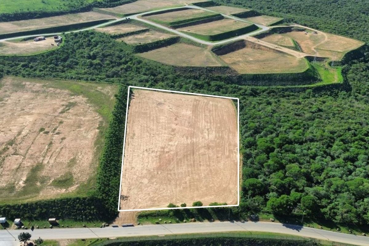 Aerial view of a cleared industrial plot with direct road access, surrounded by natural vegetation and adjacent development infrastructure.