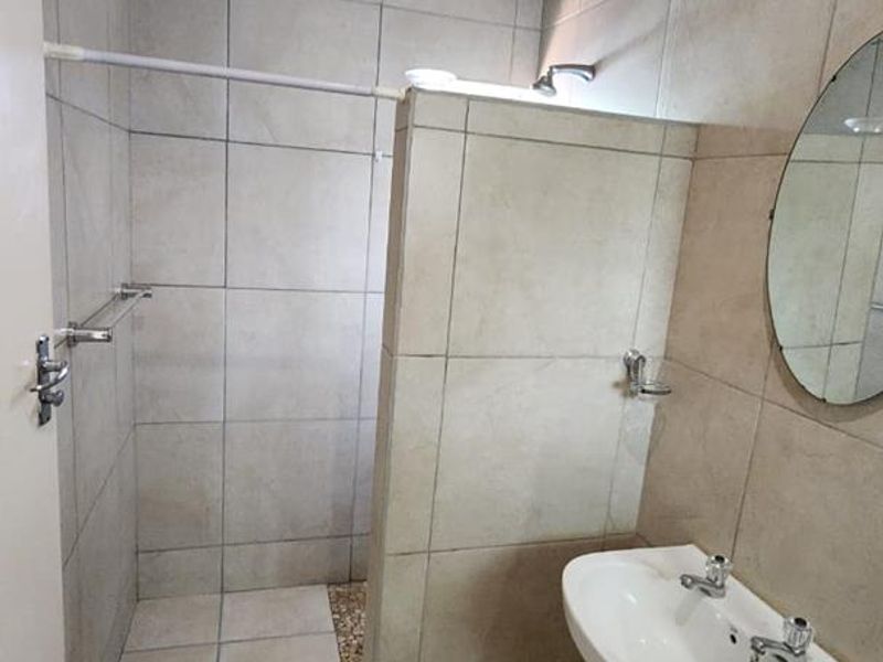 A functional bathroom featuring a pedestal basin, tiled shower enclosure, and neutral wall tiling, offering a clean and practical space.