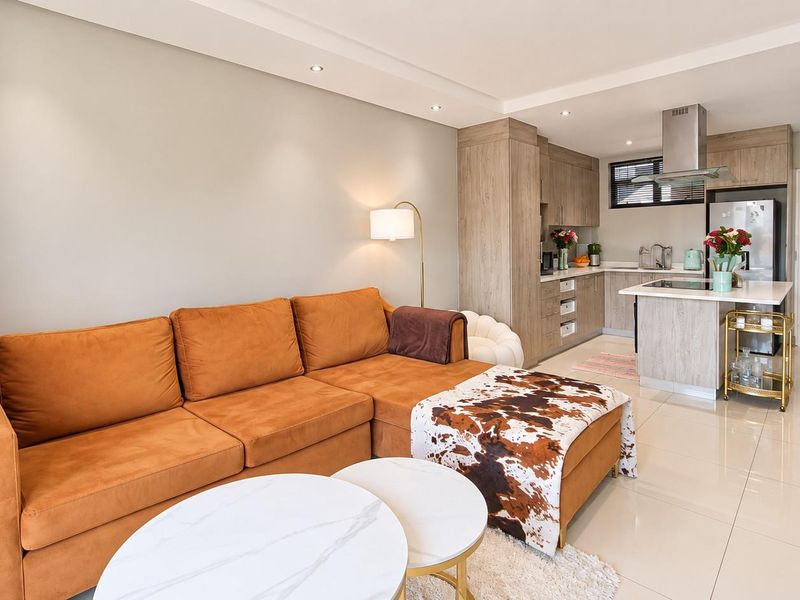 Modern open-plan living area featuring a contemporary kitchen with island, sleek cabinetry, and tiled flooring throughout, creating a bright and functional living space.