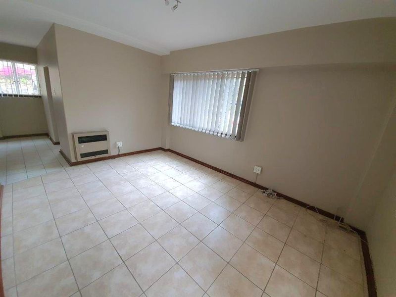 An empty living room featuring neutral wall paint, ceramic tiled flooring, and vertical window blinds.