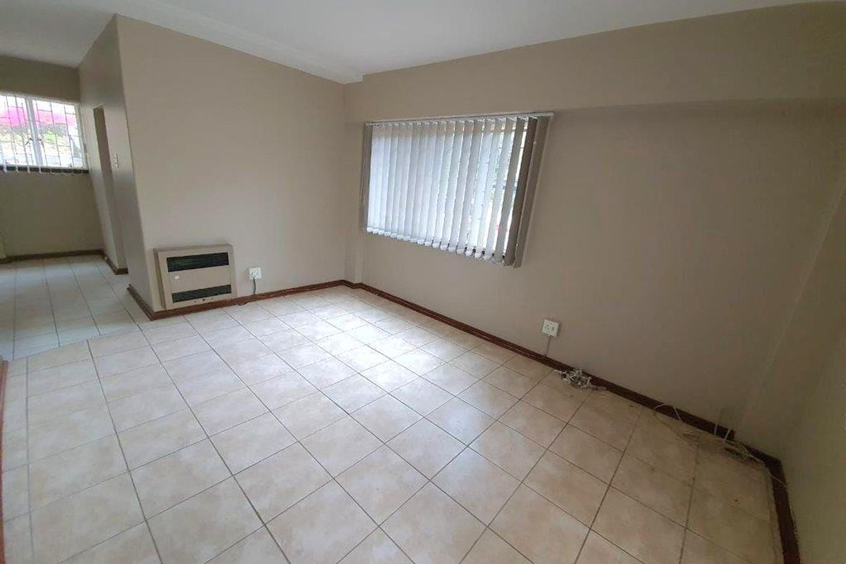 An empty living room featuring neutral wall paint, ceramic tiled flooring, and vertical window blinds.