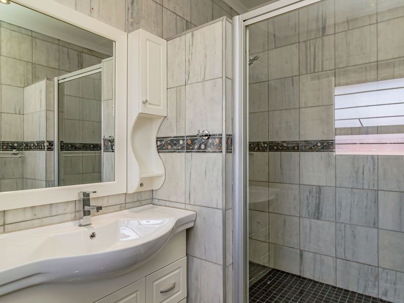 A clean bathroom featuring a vanity cabinet with a basin, a wall-mounted mirror, and a glass-enclosed shower with tiled finishes.
