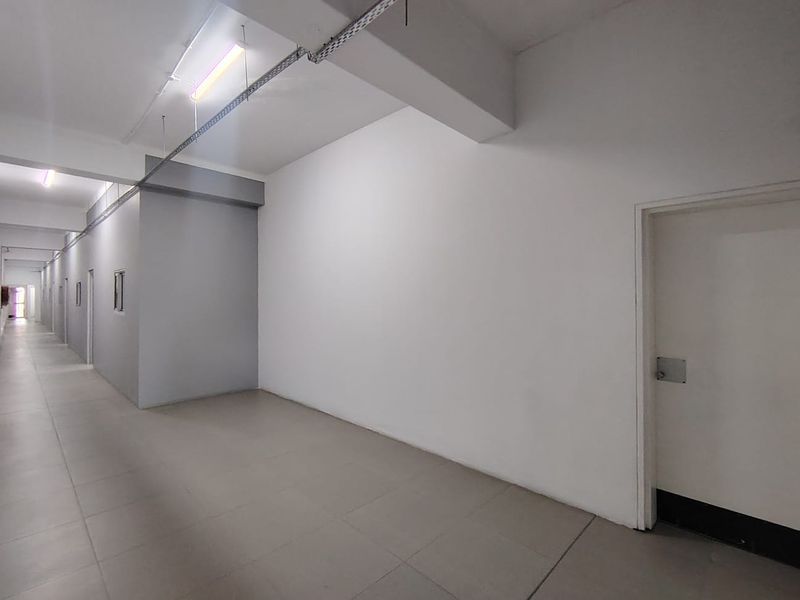 A clean, minimalist office hallway featuring tiled flooring, exposed industrial-style cable management, and multiple access doors.