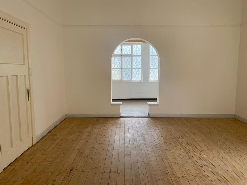 An empty bedroom featuring polished timber flooring, a distinctive arched window, and classic picture rail detailing.