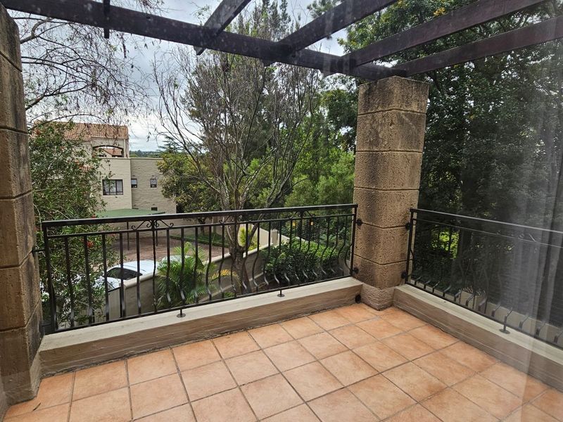 A covered balcony featuring tiled flooring, stone pillars, and a timber pergola, offering an open outdoor space with wrought iron railings.