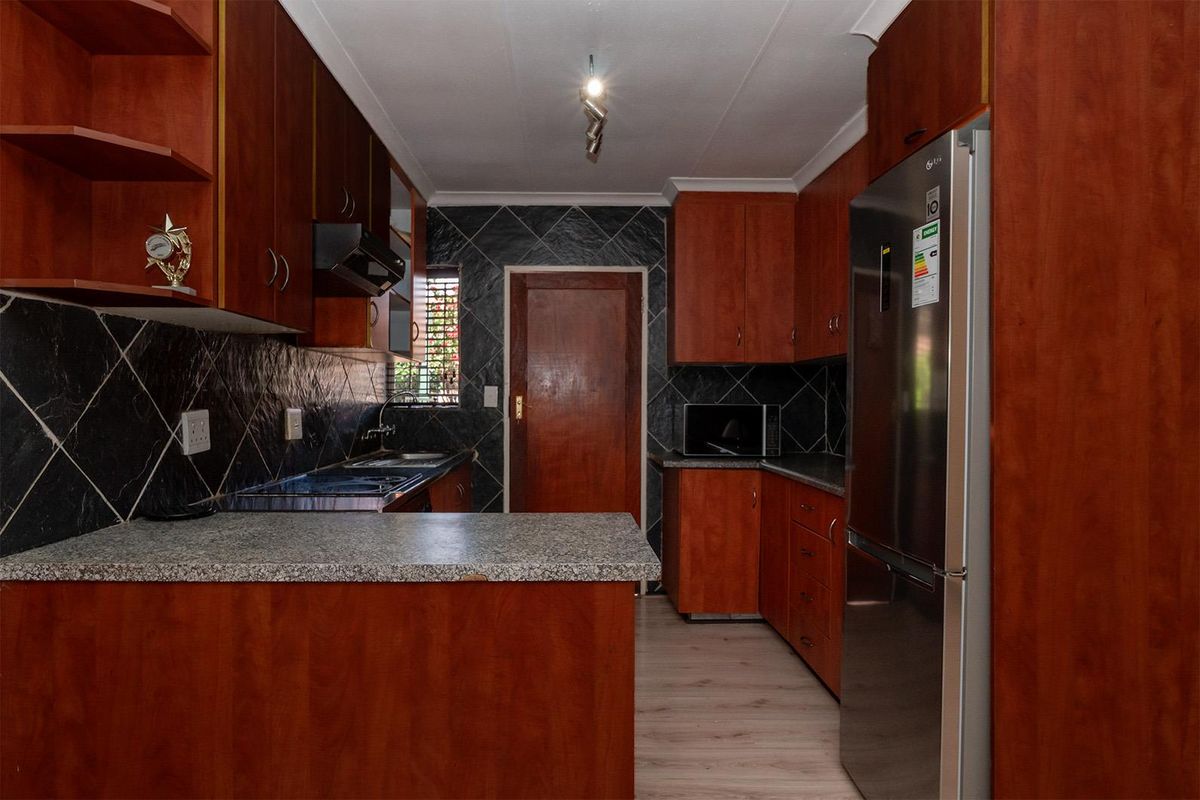 A functional kitchen featuring wood-finish cabinetry, dark tiled splashbacks, granite-look countertops, and integrated lighting.