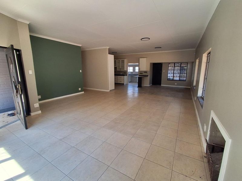 Spacious open-plan living area featuring tiled flooring, a built-in fireplace, and a connected kitchen space with cabinetry and a breakfast counter.