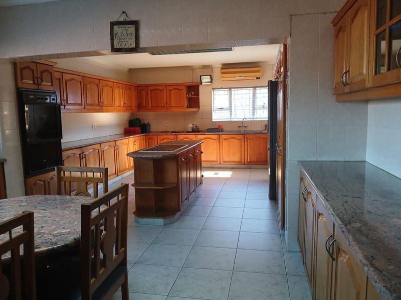 Spacious kitchen featuring extensive wooden cabinetry, granite countertops, a central island, and tiled flooring, offering a functional layout with ample storage space.