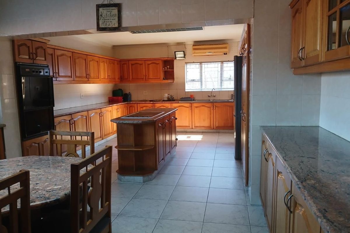 Spacious kitchen featuring extensive wooden cabinetry, granite countertops, a central island, and tiled flooring, offering a functional layout with ample storage space.