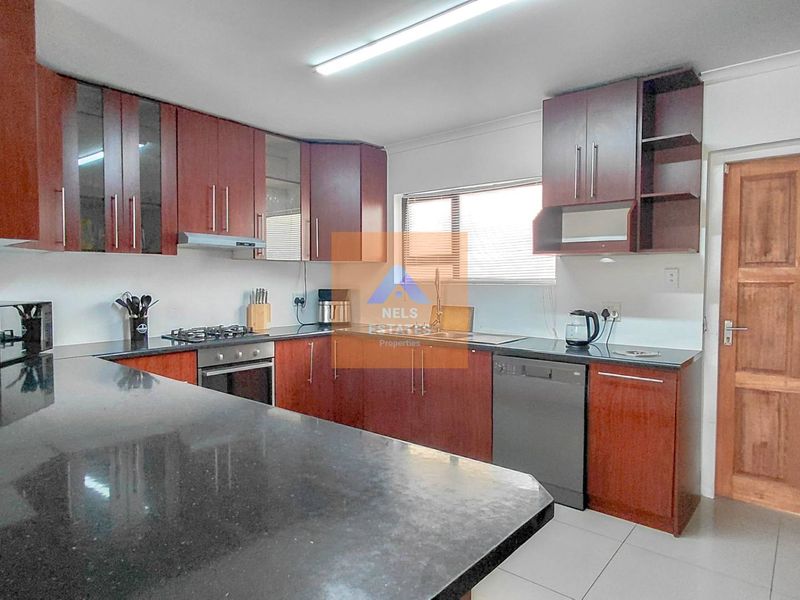 A functional kitchen featuring dark wood cabinetry, granite countertops, a gas hob, built-in oven, and tiled flooring with direct access to an exterior door.