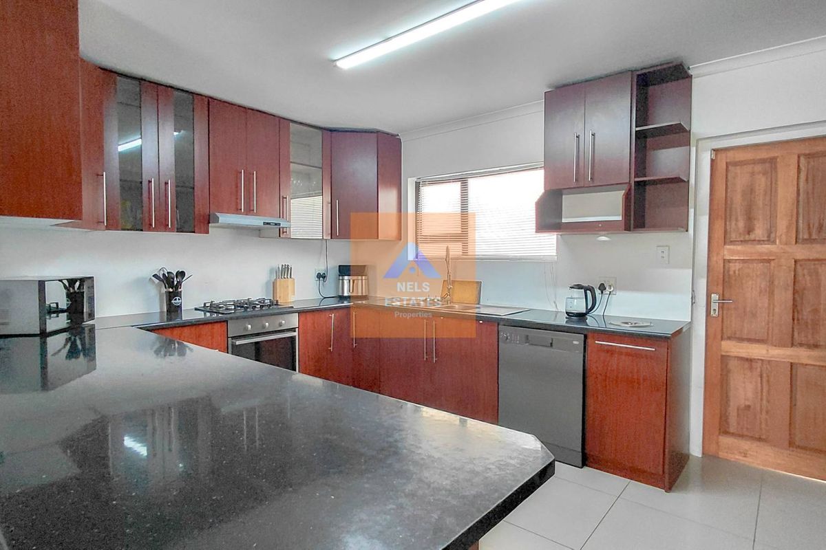 A functional kitchen featuring dark wood cabinetry, granite countertops, a gas hob, built-in oven, and tiled flooring with direct access to an exterior door.