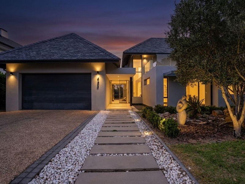 Modern front facade featuring a double garage, paved walkway, and elegant exterior lighting at dusk.