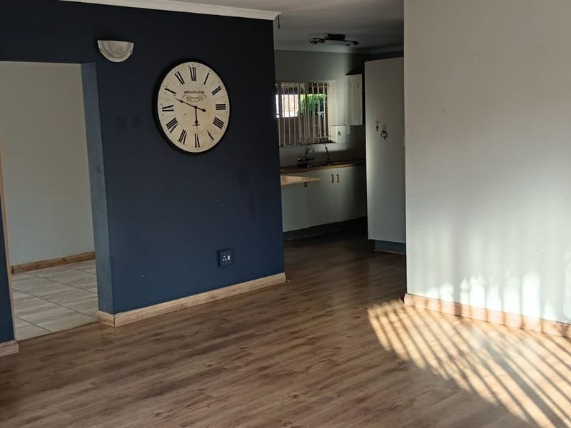 An open-plan living area featuring laminate flooring and a view into the adjacent kitchen space with built-in cabinetry.