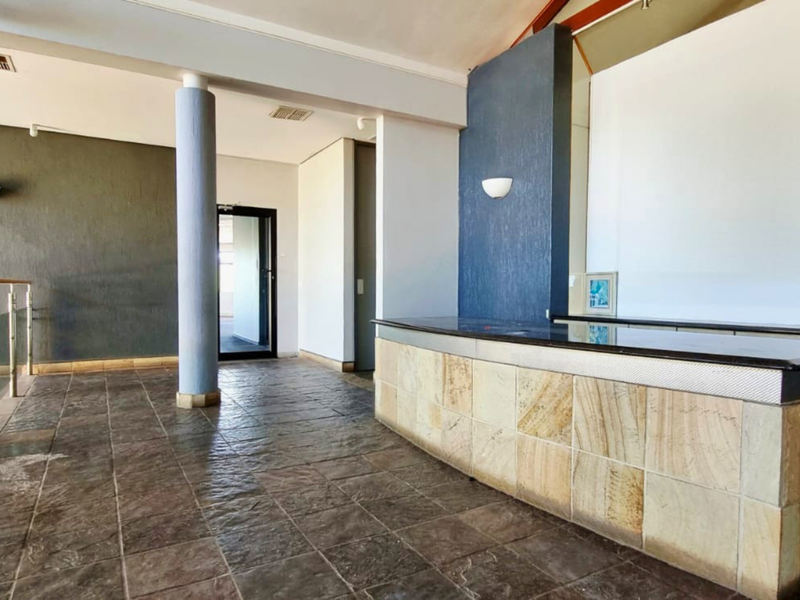 Spacious office reception area featuring a built-in stone-clad desk, tiled flooring, and modern architectural accents, providing a professional and welcoming entrance.
