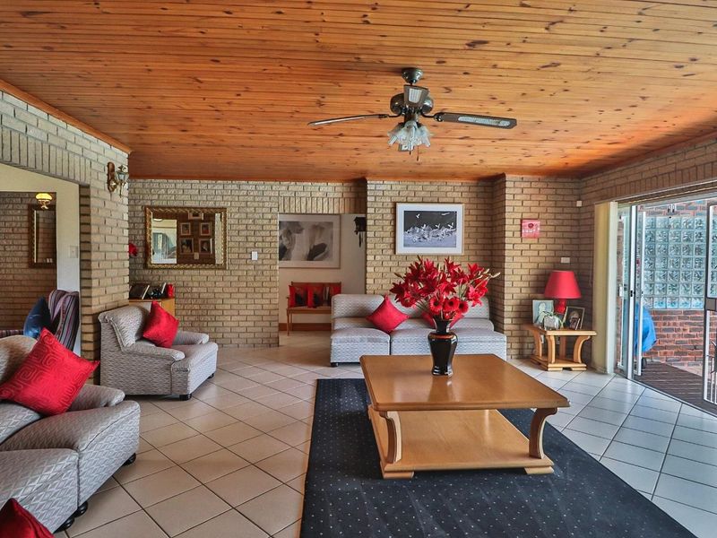 Spacious living room featuring exposed brick walls, a warm timber ceiling, ceramic tiled flooring, and direct access to an outdoor patio area.