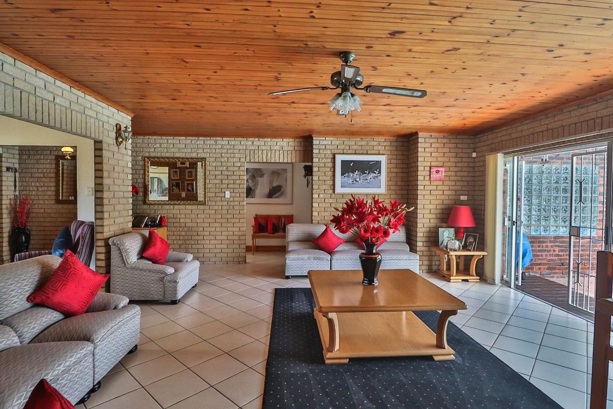 Spacious living room featuring exposed brick walls, a warm timber ceiling, ceramic tiled flooring, and direct access to an outdoor patio area.