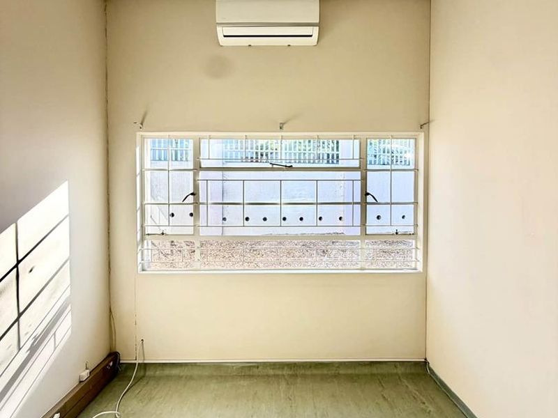 A vacant office space featuring a suspended ceiling, wall-mounted air conditioning unit, and security-fitted windows with vinyl flooring.