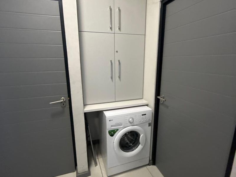 A compact laundry area featuring built-in overhead cabinetry and tiled flooring, positioned between two internal doors.