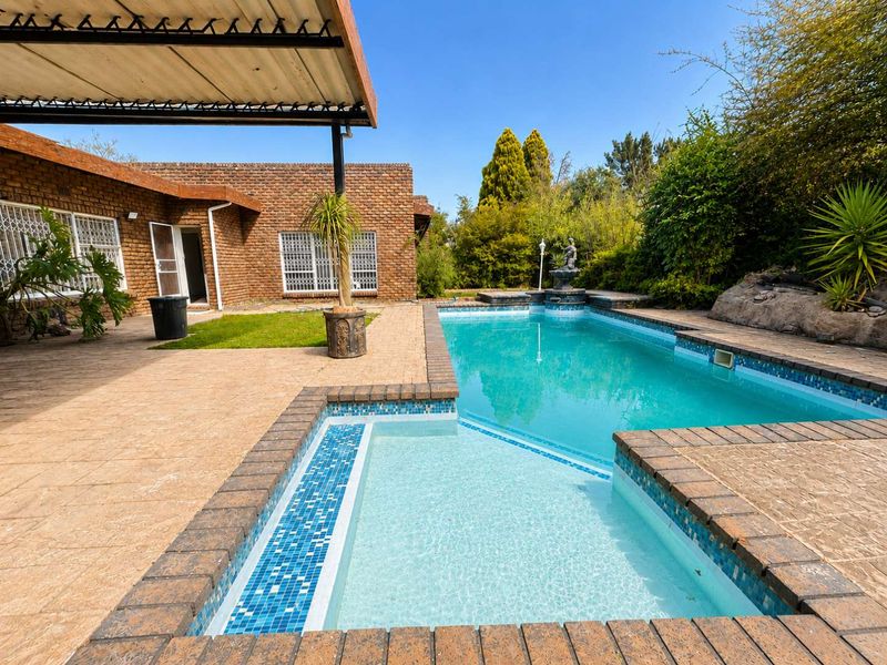 Outdoor pool area featuring a swimming pool with tiled coping, brick paved surround, and a covered patio area attached to the main brick house.