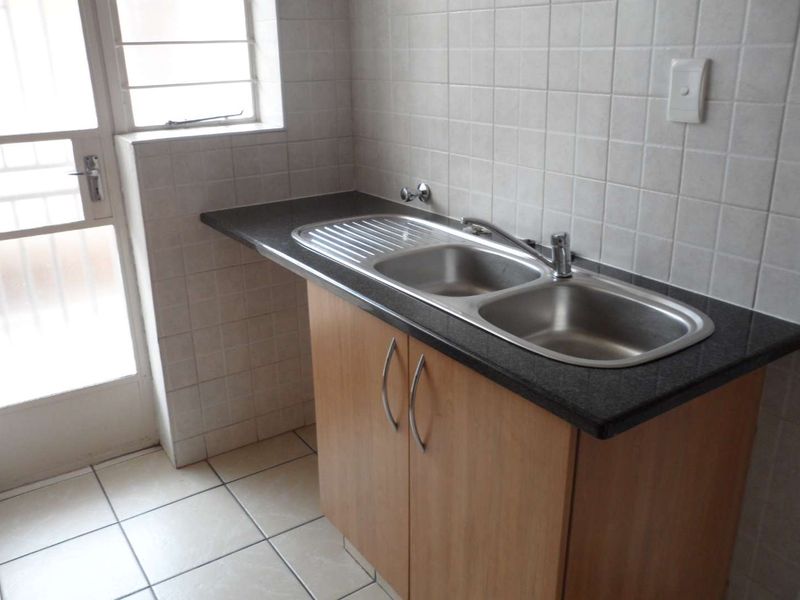 A functional laundry area featuring a stainless steel double sink, laminate countertop, base cabinetry, and tiled splashback with direct access to an exterior door.