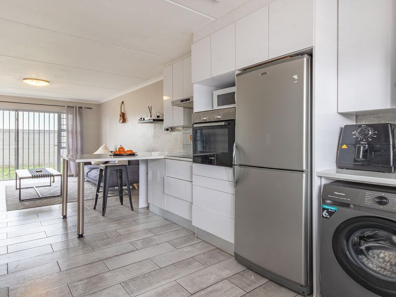 Open-plan living area featuring a modern kitchen with built-in cabinetry, oven, and extractor fan, flowing into a lounge with sliding door access to the exterior.