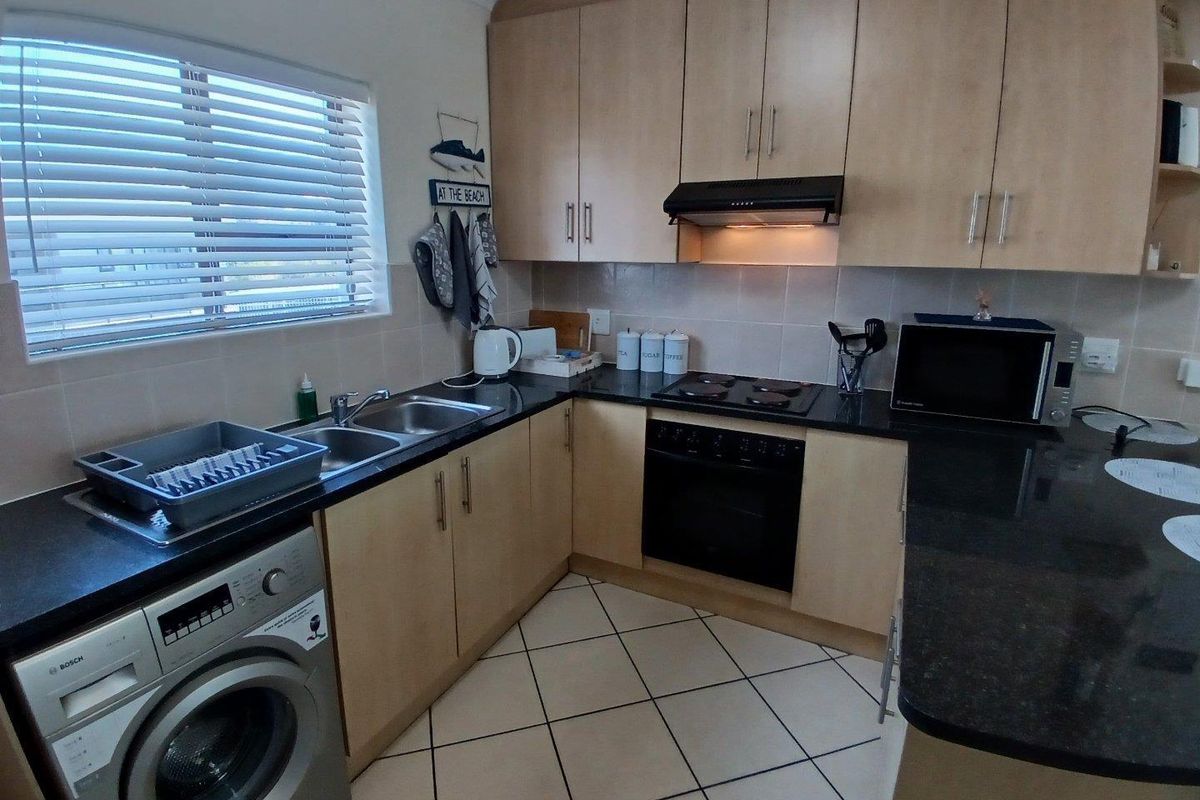 Functional kitchen featuring light wood cabinetry, dark granite countertops, tiled flooring, and integrated appliances including an oven and hob.