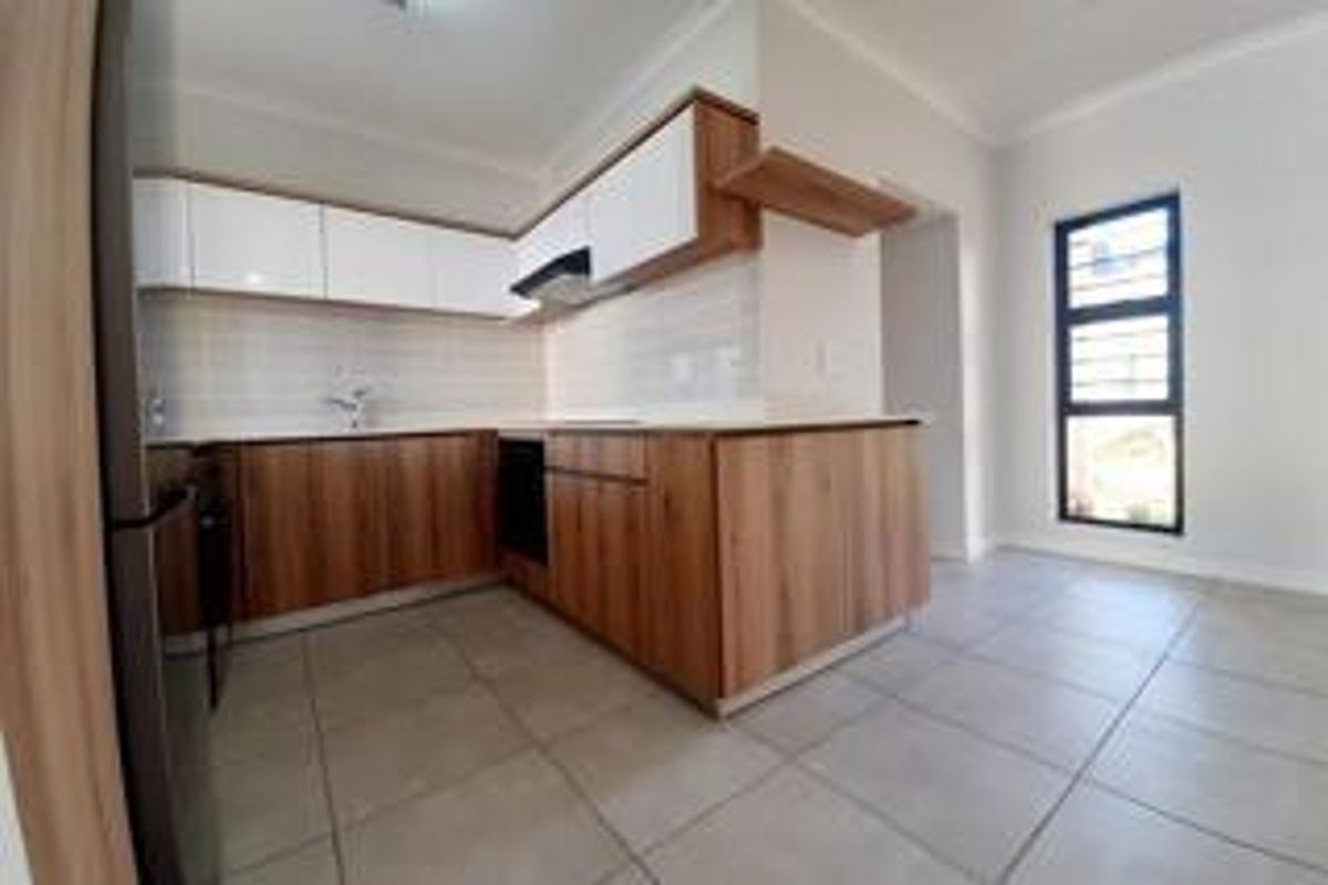 Modern kitchen featuring wood-grain cabinetry, white upper cabinets, tiled backsplash, and integrated oven, set in an open-plan layout with neutral floor tiles.