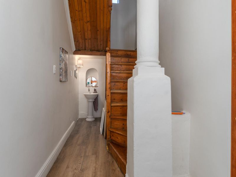A hallway featuring a wooden staircase, timber ceiling detail, and a small alcove containing a pedestal basin.