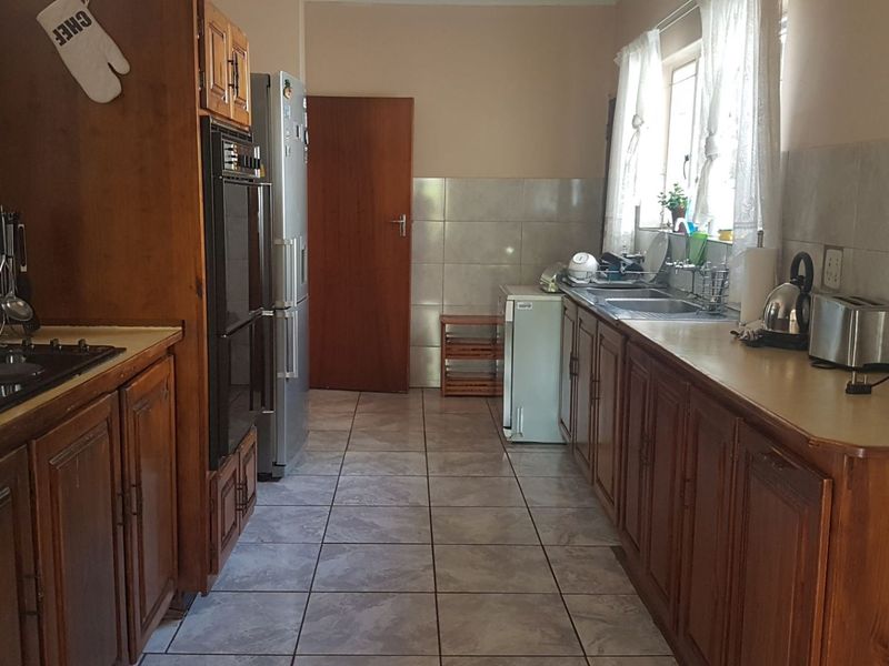 A functional galley-style kitchen featuring wooden cabinetry, an electric hob, built-in oven, and tiled finishes throughout.
